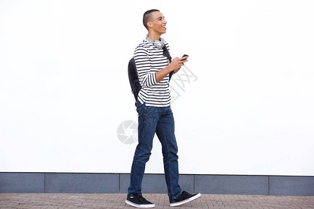 快乐的青年男子用手提袋和手机在白墙上行走的图片
