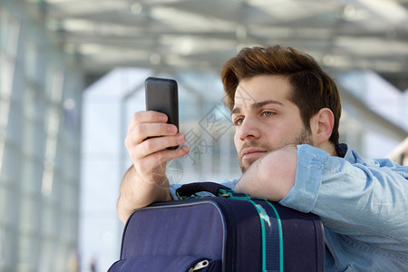 一位年轻旅行者在车站等候并看手机的近距图片
