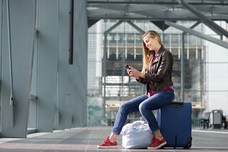 一位坐在手提箱上看着手机微笑着的年轻女图片