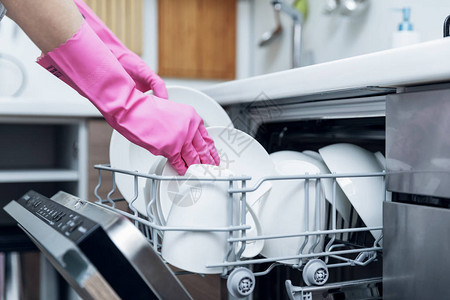 家庭主妇从家里厨房的洗碗机中取出干净的餐具图片