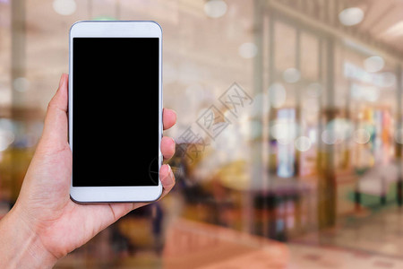 手持白色手机在模糊的咖啡馆背景图片