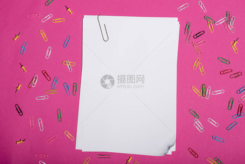 在粉红色上隔离的空白皮书和彩色纸夹的顶部视图图片