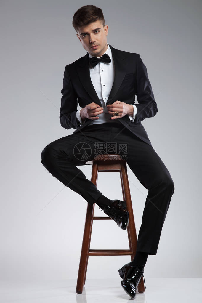 坐在木椅子上用浅灰色背景扣着黑西装图片