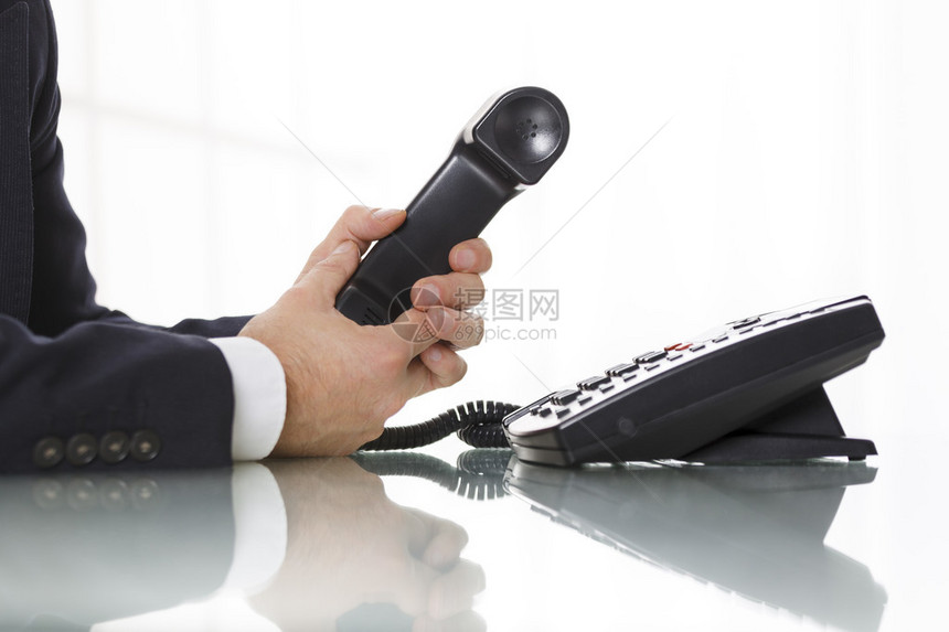 深灰色西装的商人拿着黑色固定电话的接收器关闭他的手臂和白色背景上的电话商业图片