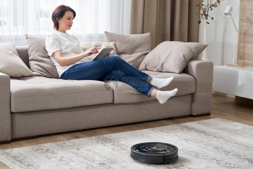 女人在沙发上休息时用机器人真空吸尘器清图片