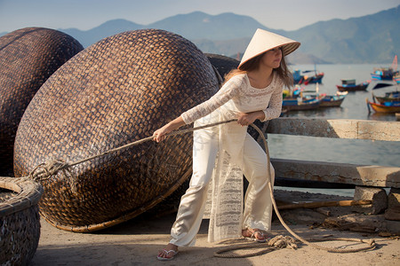 身穿越南白长裙和帽子的金发小金发女孩在围堤上拉绳子图片
