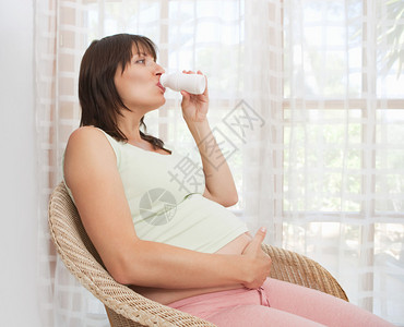 一位年轻孕妇坐在家里的大法式玻璃门旁图片
