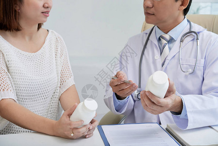 医生穿着白大褂坐在办公桌前给年轻病人开药图片