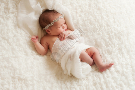 一个戴着水钻头带的睡觉8天大的新生女婴的俯视图她裹着白色的薄纱图片