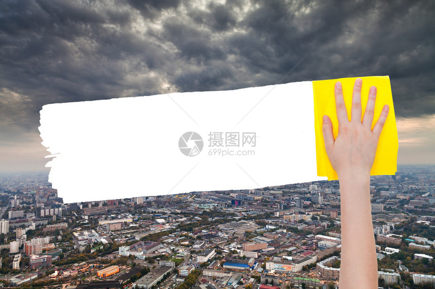 手从图象上用黄色抹布删除城市上空的暴云图片