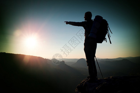 日出与反转深秋山谷上方的悬崖与顶部的导游徒步旅行者图片