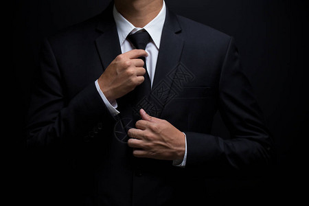 黑西装的男人和调整他的领带图片