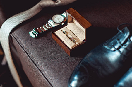 棕色木箱中的婚戒领带皮鞋和棕色沙发上的手表图片