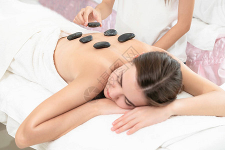 女人在spa沙龙接受专业美容师治疗师的热石按摩治疗豪华健康缓解背部压力和恢背景图片