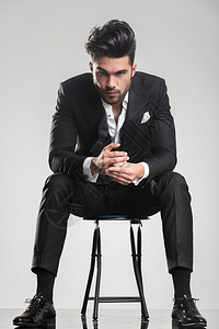 穿着晚礼服的优雅时装男坐在凳子上握图片