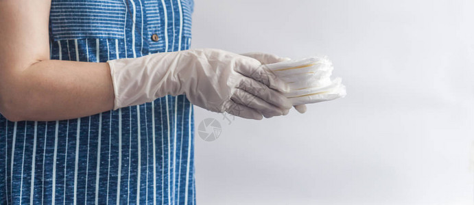 女卫生用品拿着一摞卫生巾的医疗手套的妇女反对白色背景显示女月经周期图片