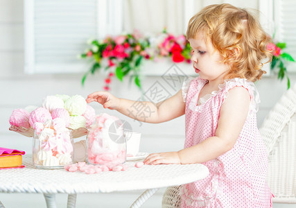 穿粉红色裙子的可爱小卷发女孩带蕾丝和圆点坐在花园的桌子上图片