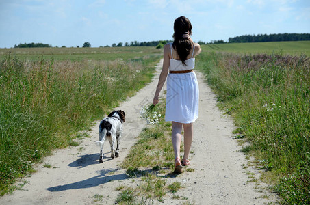 穿着白裙子的女人和她最爱的狗一起散步乡村的女模特图片