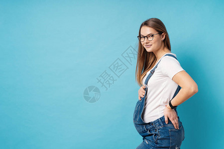 一位怀孕的年轻女士站在工作室的蓝色背景旁站着后背痛图片