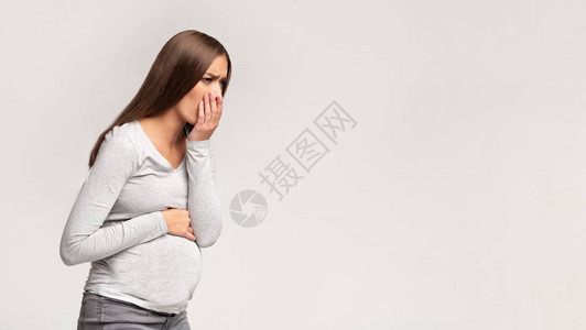 怀孕晨吐孕妇有恶心感觉不好和生病站在灰色的背景影棚拍摄图片