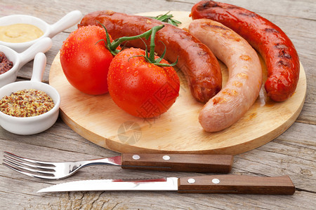 烤香肠配调味品和切菜板上的西红柿图片