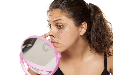 年轻女子在镜子前用手指检查鼻子图片