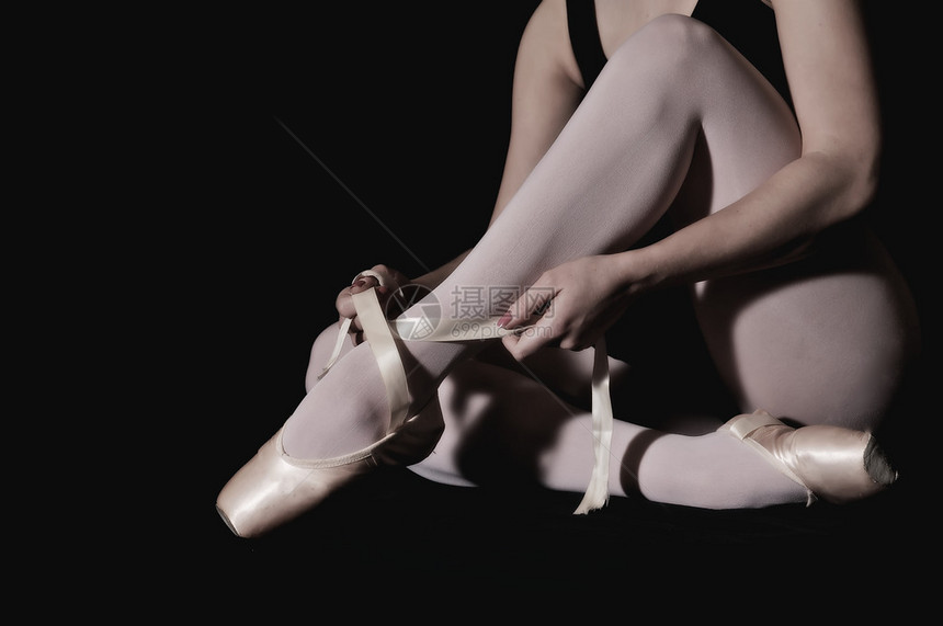 芭蕾舞演员在黑色背景下准备她的鞋子图片