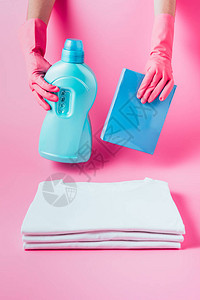 粉红色背景的一堆清洁白色T恤衫上装有洗衣液和洗衣粉的橡胶手套图片