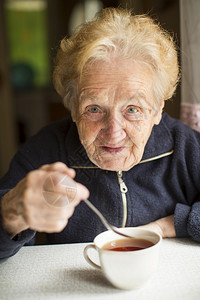 祖母坐在桌边用杯子喝茶图片