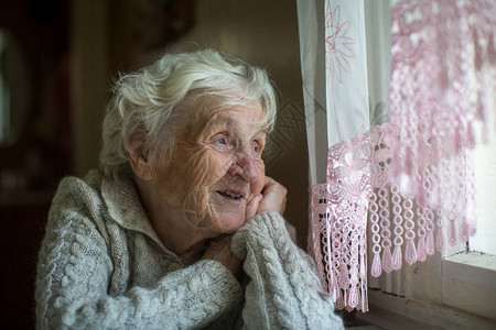 一位白头发的老年妇女坐在窗背景图片