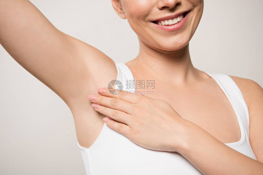 微笑着的妇女将除臭剂用在灰色隔离的下臂图片