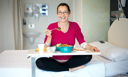 一位孕妇在医院病房吃午饭的照片该照片是图片