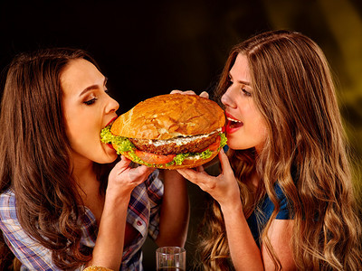 女孩持有和咬着来自不同侧面的大汉堡包图片