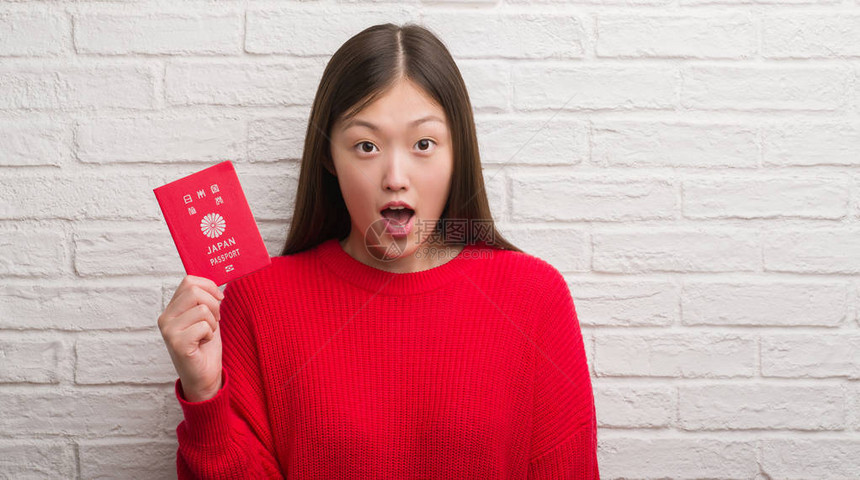 拿着日本护照的砖墙上的年轻女子惊得面目全非图片
