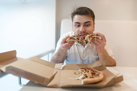留着胡子的有趣男人从纸板箱里吃披萨一个男人手里拿着一块比萨饼图片