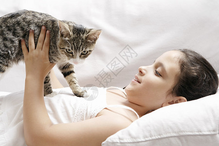 年轻女孩躺在白色沙发上时抱着小猫图片