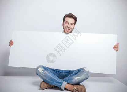微笑的年轻时尚男子拿着一个大空板坐在他的图片