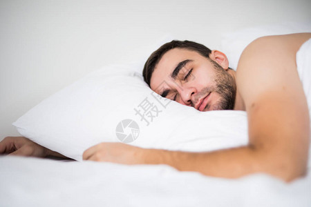 英俊的年轻人睡在白色床上用品图片