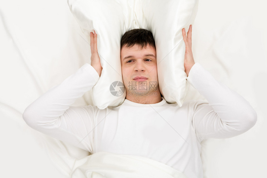 疲倦的男子用耳朵闭上枕头睁开双眼躺在床图片