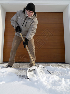 大雪后男子用铲子清理车道上的积雪图片