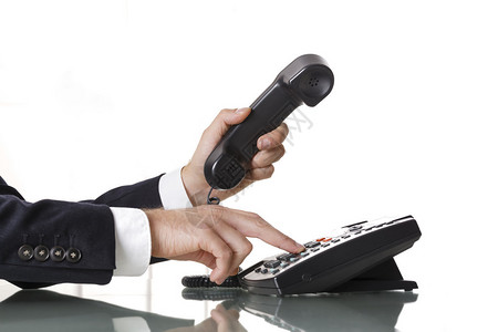 穿着深灰色西装的商人在黑色固定电话上拨打号码他的手和电话的特写镜头在白色背景商业背景图片