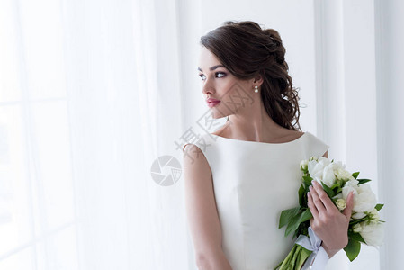 美丽新娘抱着婚礼花束看着窗图片