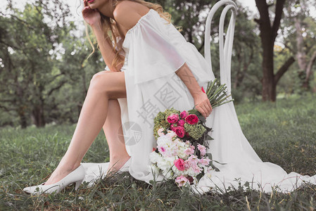 年轻新娘拿着鲜花束坐在公园的椅图片