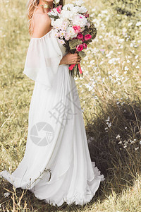 身着婚纱的年轻新娘在户外盛放一束美丽的花束图片
