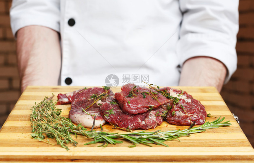 厨师拿着新鲜的猪肉牛排准备烧烤烹饪在切菜板上的生肉与迷迭香叶生猪肉在木头上图片