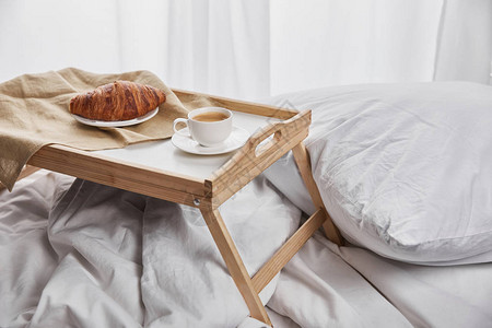 清晨在床上用枕头和枕头的木托盘上加咖啡的图片