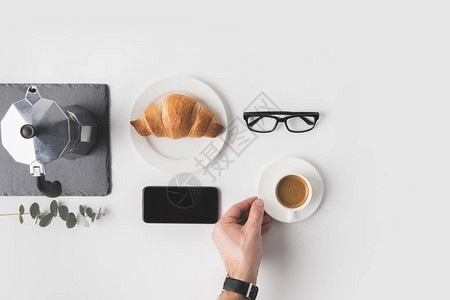 男子用智能手机眼镜和羊角面包杯咖啡在接近白面的附近早餐图片
