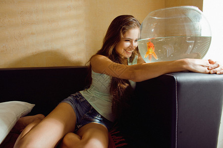 鱼缸底沙漂亮的美女在家玩金鱼阳光照背景
