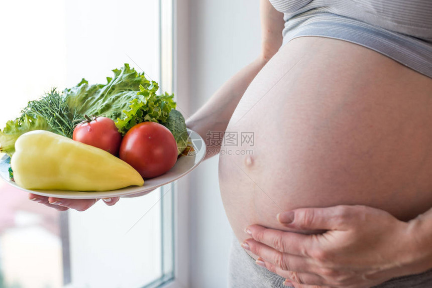 一个有肚子的孕妇手里拿着一盘蔬菜孕期体重控制和健图片