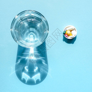 在一个透明的玻璃杯和蓝色表面盖上一剂药高清图片